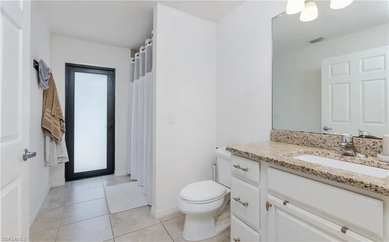 Bathroom featuring a white vanity with a light-toned stone countertop and integrated sink, a frameless mirror, and a three-light fixture
