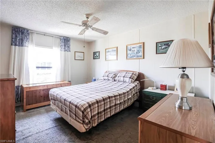 Bedroom with dark colored carpet, ceiling fan, and a textured ceiling