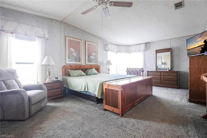 Bedroom with ceiling fan, carpet flooring, vaulted ceiling, and a textured ceiling