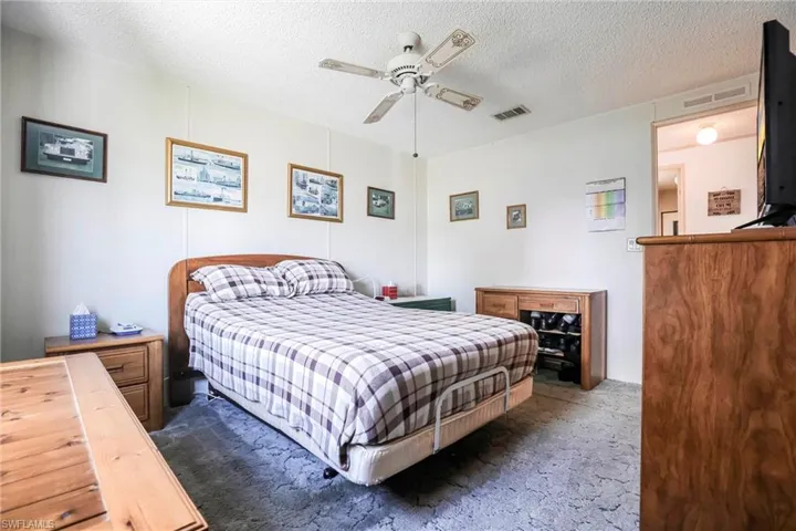 Bedroom with ceiling fan, a textured ceiling, and dark colored carpet