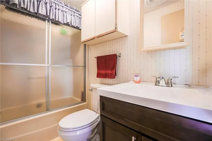 Full bathroom with vanity, shower / bath combination with glass door, and toilet