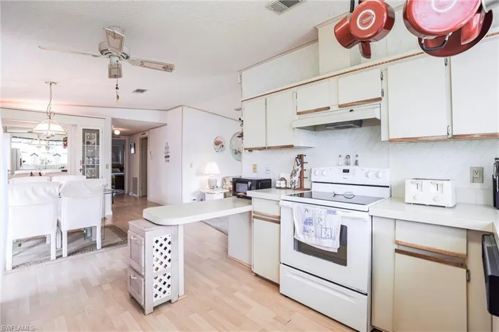 Kitchen with white electric stove, white cabinetry, light hardwood / wood-style flooring, and decorative light fixtures