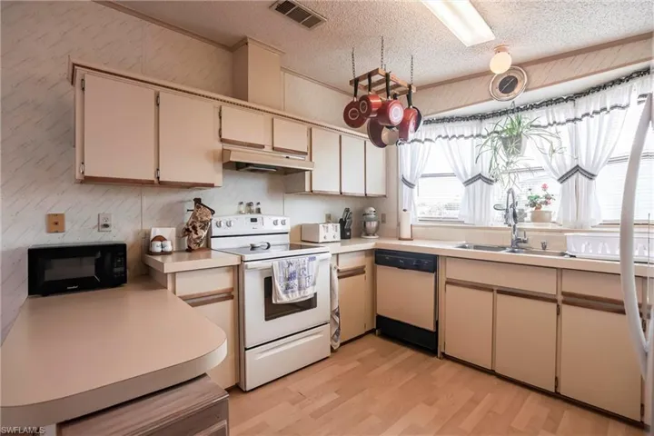 Kitchen featuring sink, light hardwood / wood-style flooring, a textured ceiling, white appliances, and cream cabinets