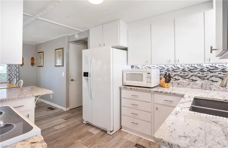 Kitchen with decorative backsplash, white cabinetry, white appliances, and light wood-style floors