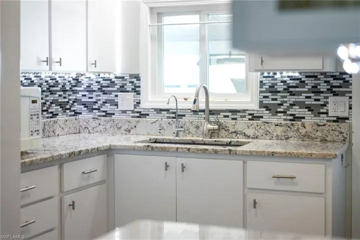 Kitchen with white cabinetry, light stone counters, and white microwave