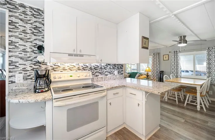 Kitchen with electric stove, light wood finished floors, under cabinet range hood, a peninsula, and white cabinets