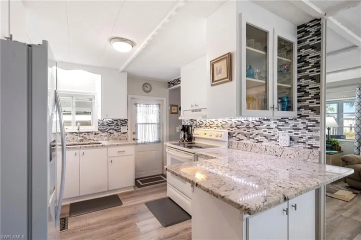 Kitchen featuring white appliances, white cabinetry, a peninsula, light stone counters, and light wood-style flooring