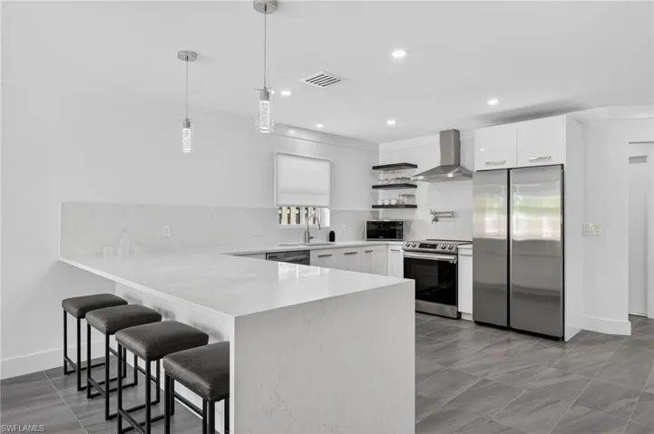 Kitchen featuring open shelves, a breakfast bar area, appliances with stainless steel finishes, decorative backsplash, and white cabinetry