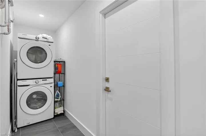 Washroom with stacked washer and clothes dryer and dark tile patterned floors