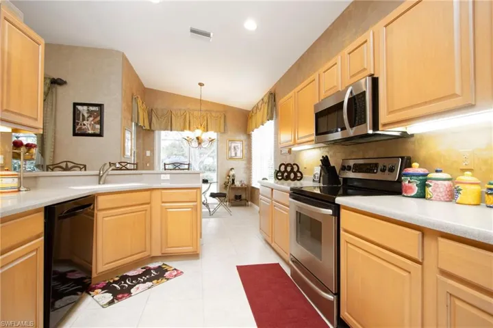 Kitchen with pendant lighting, light brown cabinetry, vaulted ceiling, appliances with stainless steel finishes, and sink