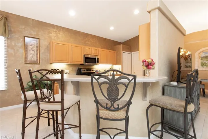 Kitchen with light brown cabinetry, kitchen peninsula, stainless steel appliances, and a breakfast bar area