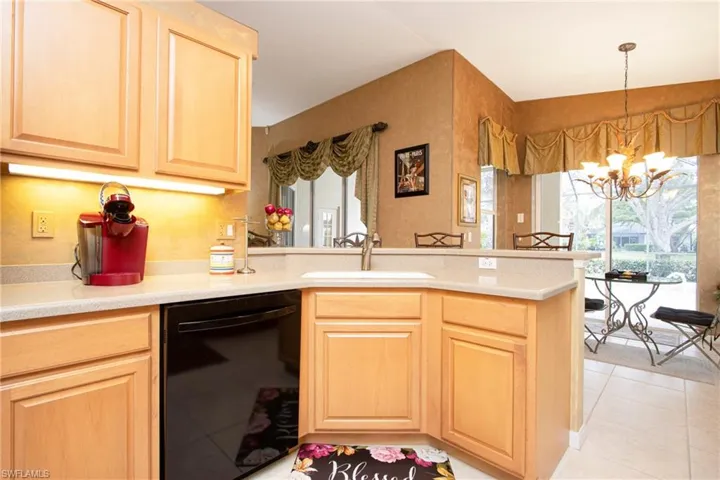 Kitchen with black dishwasher, light tile patterned floors, sink, decorative light fixtures, and kitchen peninsula
