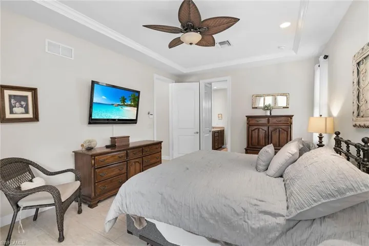 Bedroom featuring connected bathroom, recessed lighting, ornamental molding, a ceiling fan, and a tray ceiling