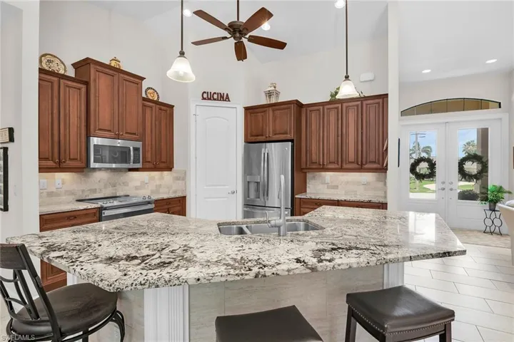 Kitchen with stainless steel appliances, a breakfast bar area, a ceiling fan, hanging light fixtures, and high vaulted ceiling