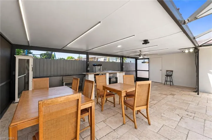 Covered outdoor patio featuring stone-tile flooring, built-in bar area, recessed linear lighting, and ceiling fan