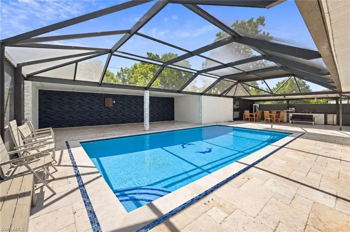 Screened-in outdoor living area featuring a large inground pool with tiled steps, stone-finish paver deck, and textured accent wall