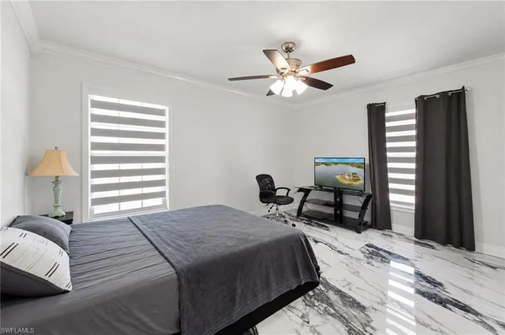 Polished stone-finish flooring with high-contrast veining, dual windows with banded roller shades, and a multi-blade ceiling fan with integrated light fixture