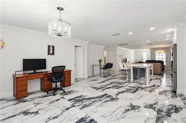 Large-format patterned tile flooring, central kitchen island with an integrated beverage refrigerator, recessed lighting, and a decorative crystal-style chandelier