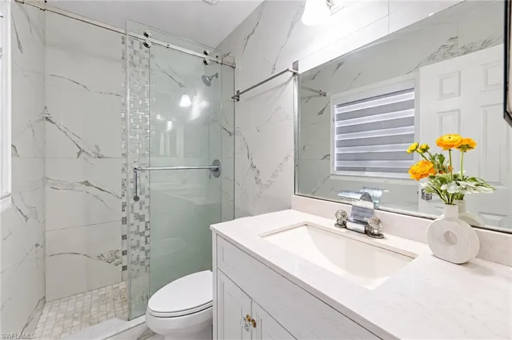 Bathroom featuring a glass-enclosed shower with floor-to-ceiling tile, vanity with a light-toned countertop, integrated sink, and expansive wall-mounted mirror