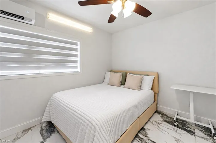 Room featuring stone-patterned tile flooring, a wall-mounted ductless air conditioning unit, a linear LED light fixture, and a ceiling fan with integrated lighting