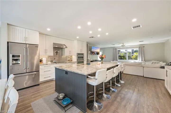 Kitchen featuring stainless steel appliances, light stone countertops, a large island, open floor plan, and dark wood finished floors