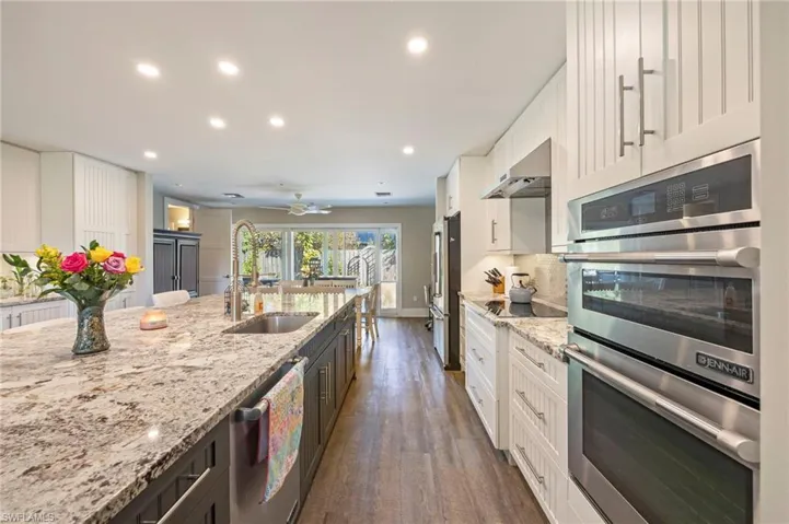 Dual tone kitchen featuring stainless steel appliances, dark wood-style floors, recessed lighting, light stone countertops, and ceiling fan