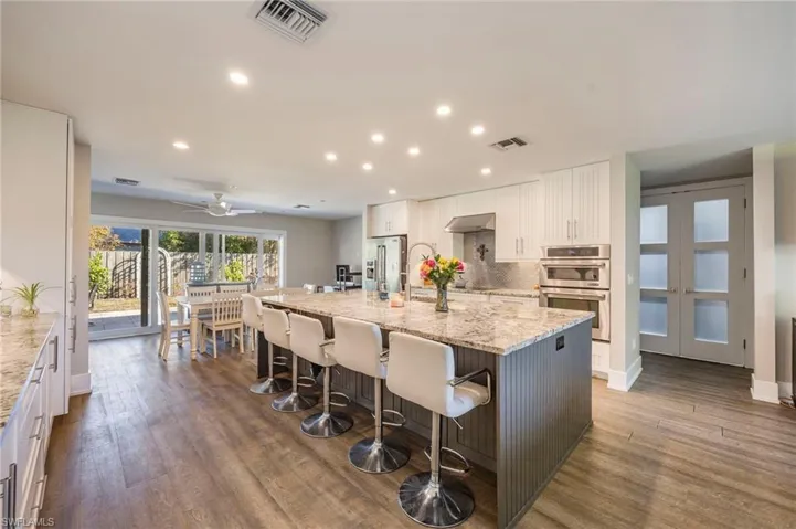 Two tone kitchen with a large island with sink, a breakfast bar, dual tone cabinets, light stone counters, and dark wood-style floors