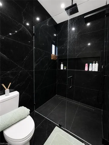 Walk-in shower featuring full-height black stone-look tile, a frameless glass enclosure, and a built-in linear drain