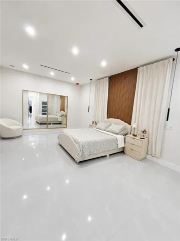 Spacious room featuring light-toned large format tile flooring, a slatted wood accent wall, recessed lighting, and full-wall mirrored closet doors with gold-toned framing