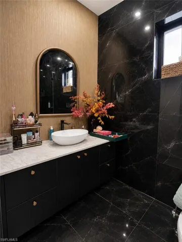 Contemporary bathroom featuring a black vanity with gold hardware, a white vessel sink, and a light-toned countertop