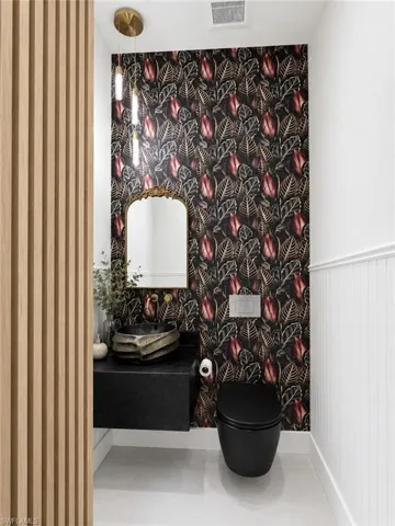 Powder room featuring a decorative accent wall with botanical wallpaper, a wall-mounted vanity with an artistic vessel sink, a gold-framed mirror, and a contemporary black toilet