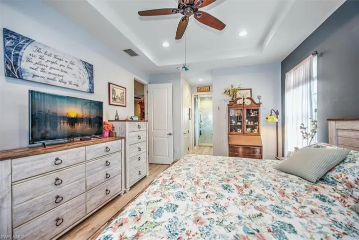 Bedroom featuring ceiling fan, light wood-type flooring, and a tray ceiling