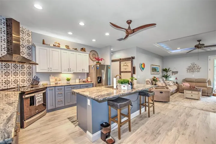 Kitchen with appliances with stainless steel finishes, light wood-type flooring, ceiling fan, sink, and wall chimney range hood