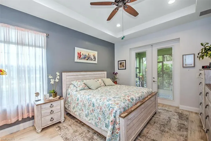 Bedroom featuring access to outside, light hardwood / wood-style flooring, a raised ceiling, and ceiling fan