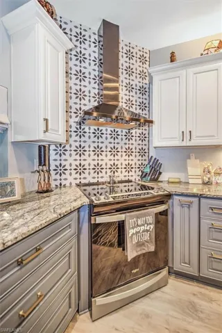 Kitchen featuring light stone countertops, stainless steel range with electric cooktop, white cabinetry, light hardwood / wood-style floors, and wall chimney range hood