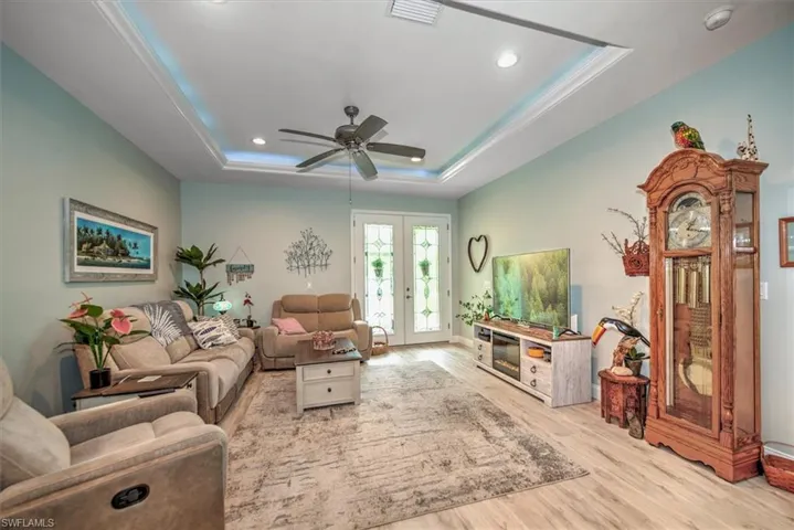 Living room with wood-style floors, french doors, ceiling fan, and a raised ceiling