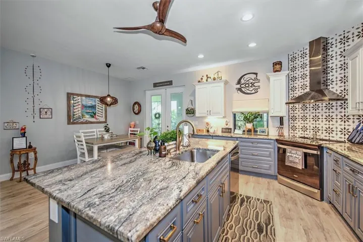 Kitchen featuring appliances with stainless steel finishes, white cabinets, wall chimney range hood, and light hardwood / wood-style flooring