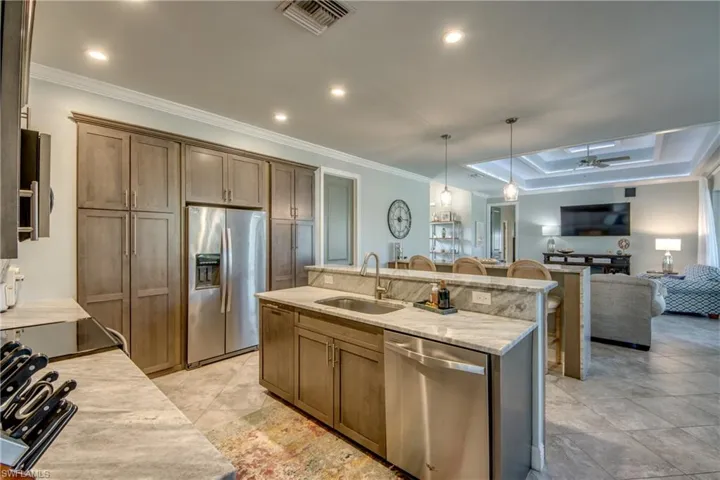 Kitchen with stainless steel appliances, open floor plan, pendant lighting, ornamental molding, and light stone counters