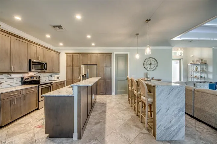 Kitchen featuring stainless steel appliances, open floor plan, light stone counters, tasteful backsplash, and decorative light fixtures