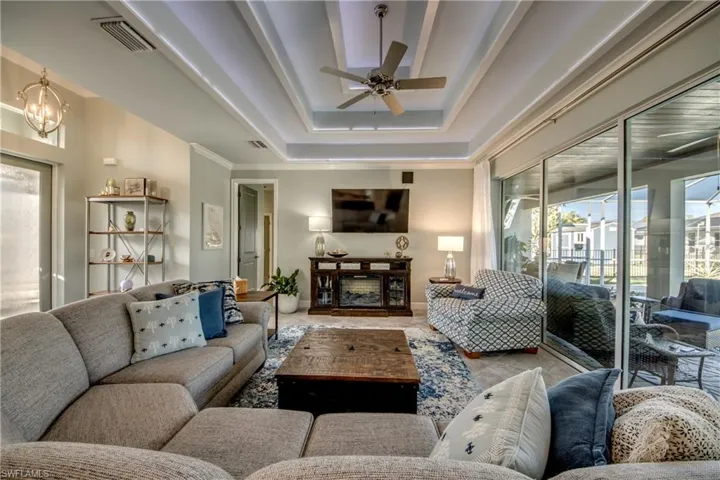 Living room with ceiling fan, ornamental molding, a tray ceiling, and a fireplace