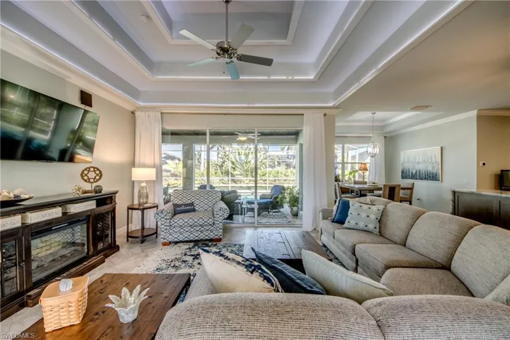 Living area with a raised ceiling, a ceiling fan, and ornamental molding