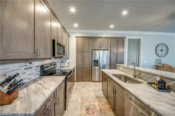 Kitchen featuring stainless steel appliances, light stone counters, recessed lighting, decorative backsplash, and ornamental molding
