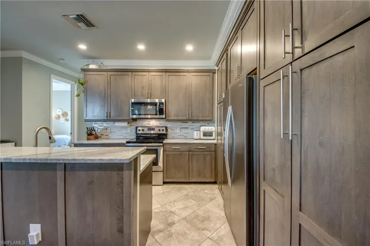 Kitchen featuring stainless steel appliances, ornamental molding, light stone countertops, tasteful backsplash, and recessed lighting