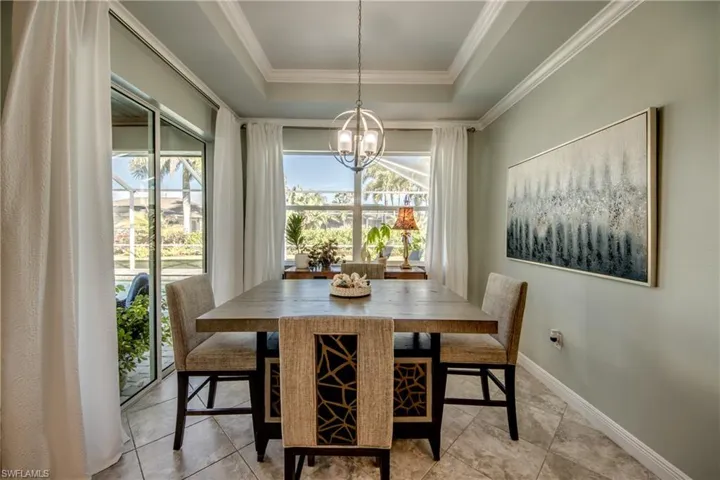 Dining room featuring a raised ceiling, hanging lights, crown molding, and light tile patterned flooring