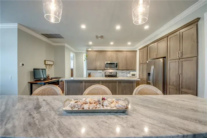 Kitchen featuring crown molding, stainless steel appliances, light stone countertops, a center island, and hanging light fixtures