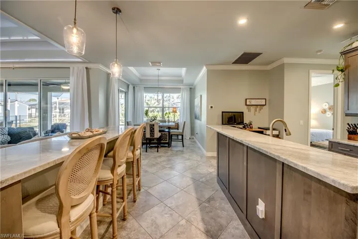 Kitchen with light stone counters, pendant lighting, ornamental molding, light tile patterned floors, and a breakfast bar area