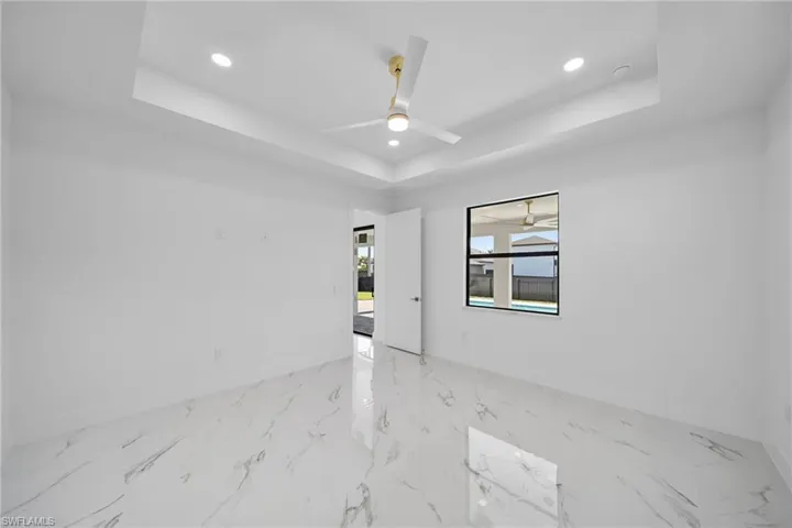 Unfurnished room with ceiling fan, a tray ceiling, and light tile flooring