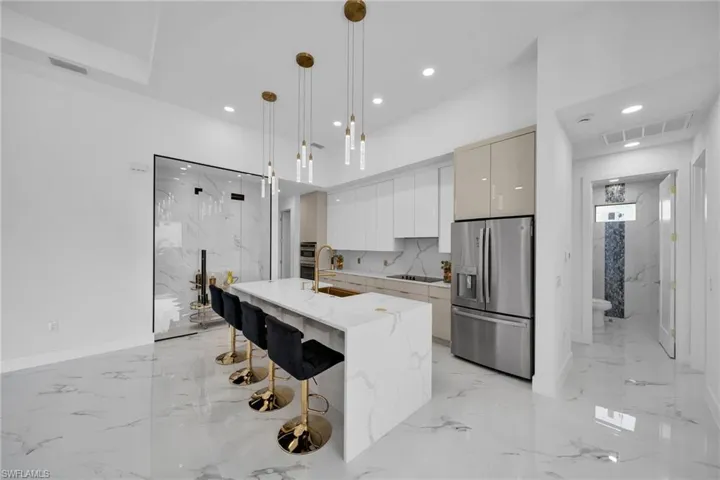 Kitchen with stainless steel fridge with ice dispenser, a center island with sink, hanging light fixtures, sink, and light tile floors
