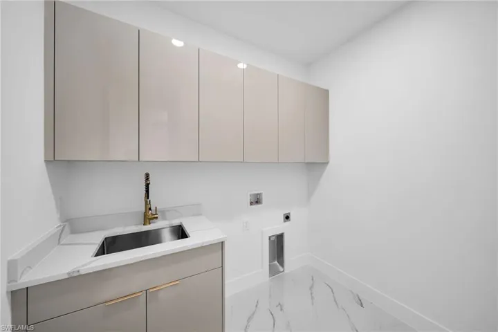 Washroom with cabinets, washer hookup, hookup for an electric dryer, sink, and light tile flooring