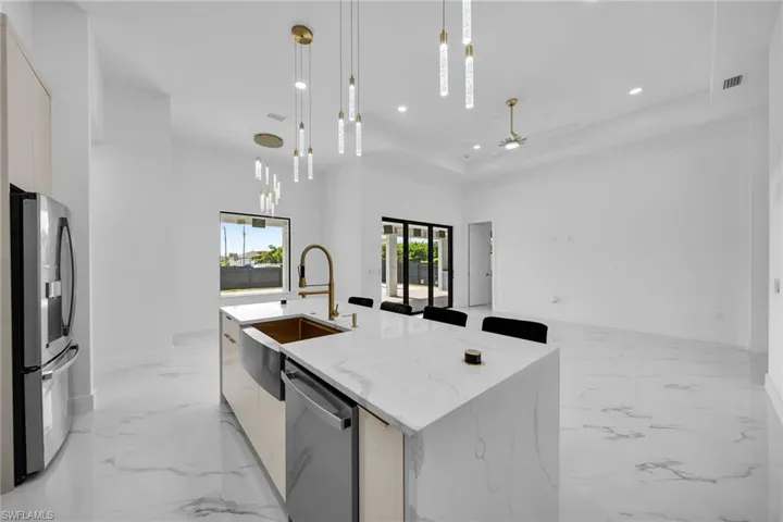 Kitchen with ceiling fan, stainless steel appliances, a center island with sink, a high ceiling, and hanging light fixtures